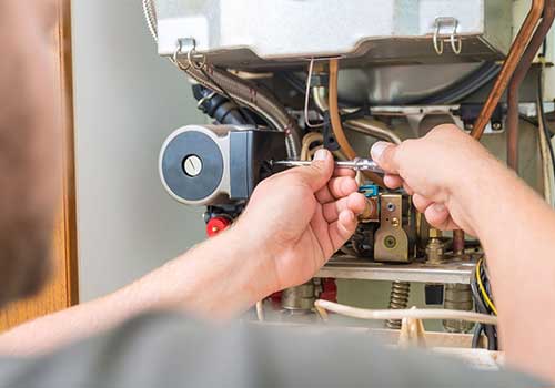 Kombi bakımı yapan sadece elleri görünen teknisyen ve kapağı sökülmüş bir kombinin iç aksamı görünüyor