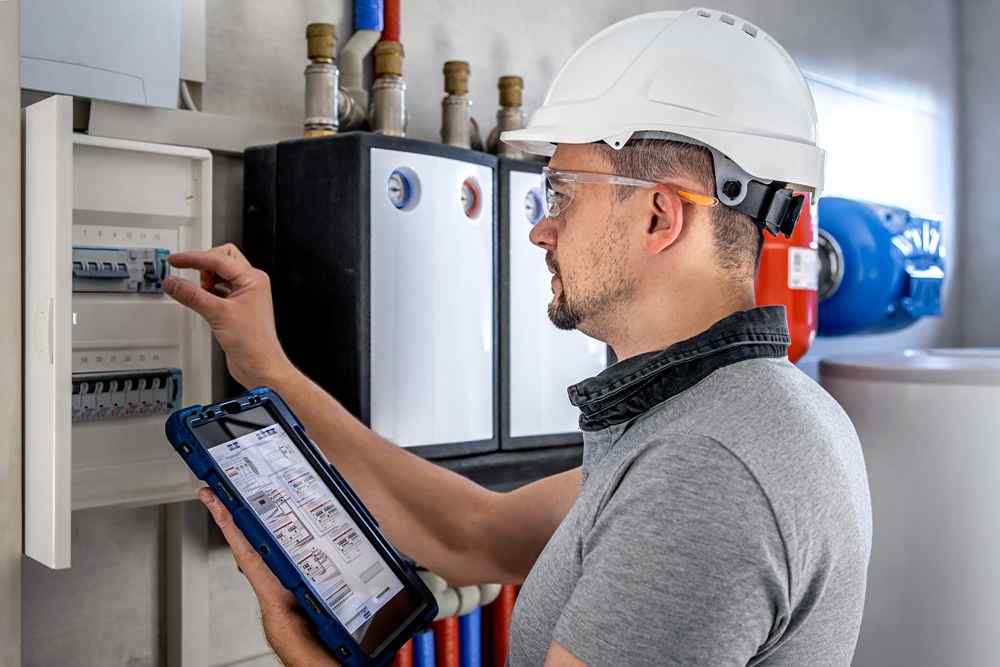 Elektrik panosunu kontrol eden kasklı Ankara Bosch Servisii teknisyeni , tablette şemaya bakıyor