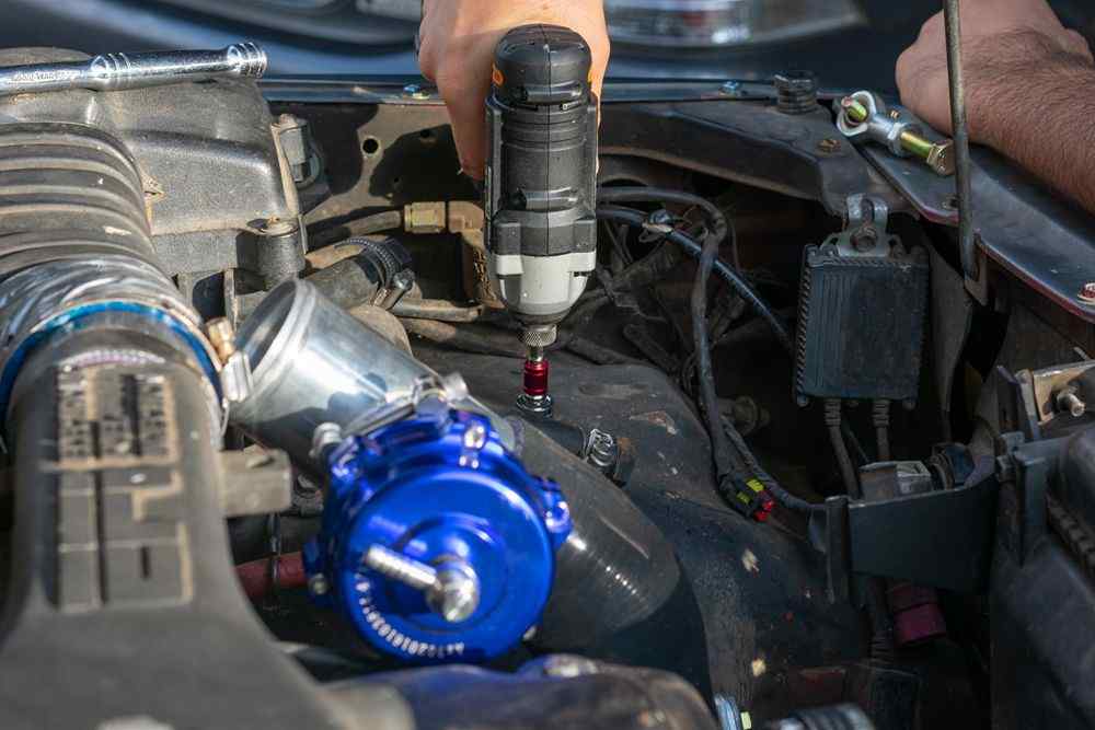 Otomobilin motor bölmesinde bir kişi elektrikli aletle parça üzerinde çalışıyor