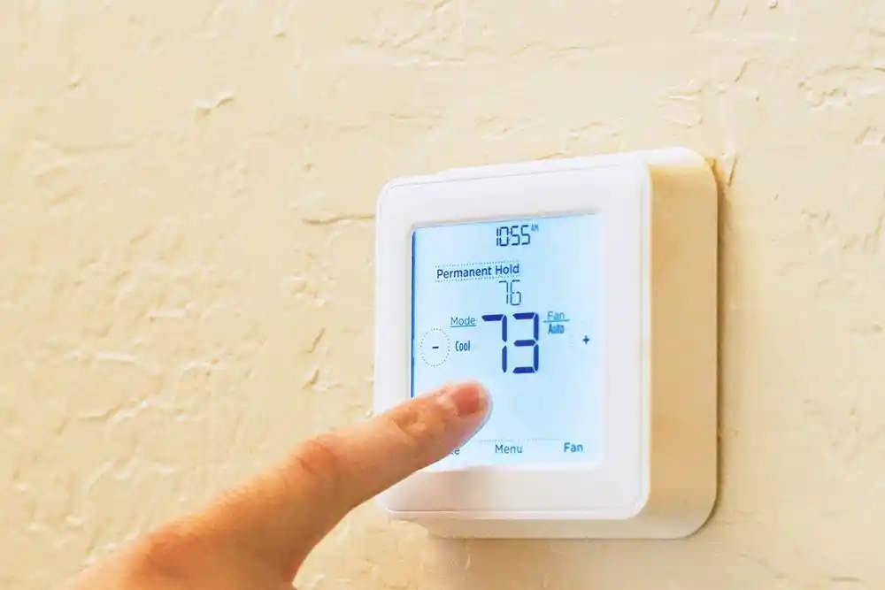 Parmağın ayarladığı duvar tipi termostatın ekranında 23 °C ve kalıcı sabitleme modu görülüyor