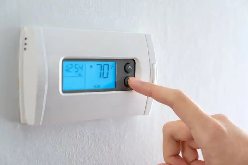 Duvara monte termostatın sıcaklık ayarı parmakla değiştiriliyor; ekranda 70 °F görünüyor