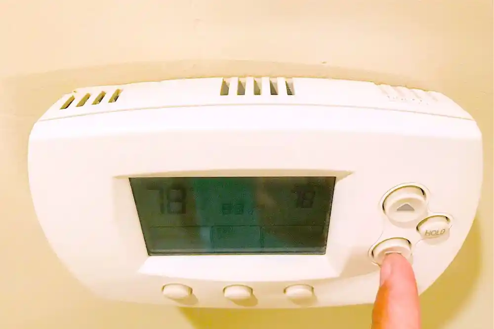 Bir parmağın beyaz duvar termostatındaki aşağı düğmesine bastığı görülüyor