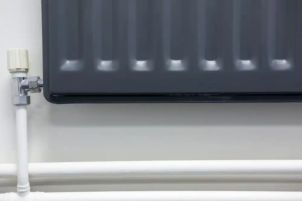 Duvara monte koyu renkli radyatör ve sol yanında bulunan vana ile borular