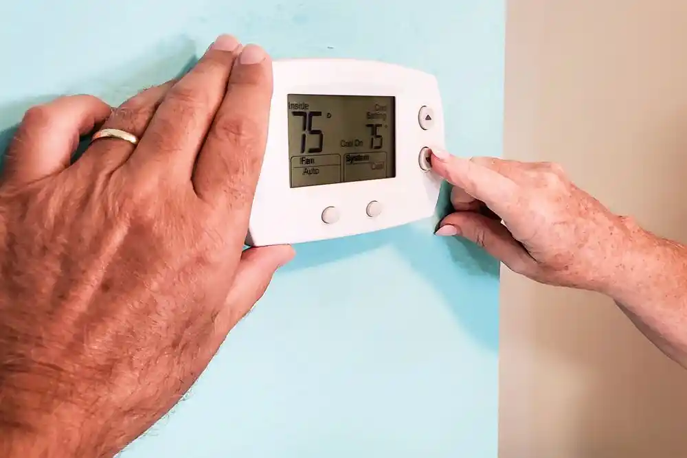 Eller, duvara monte termostatın sıcaklık ayarını 75°F’ye getiriyor