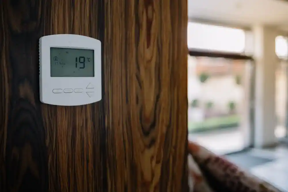 Ahşap bir duvara monte edilmiş termostat, ekranda 19 °C gösteriyor