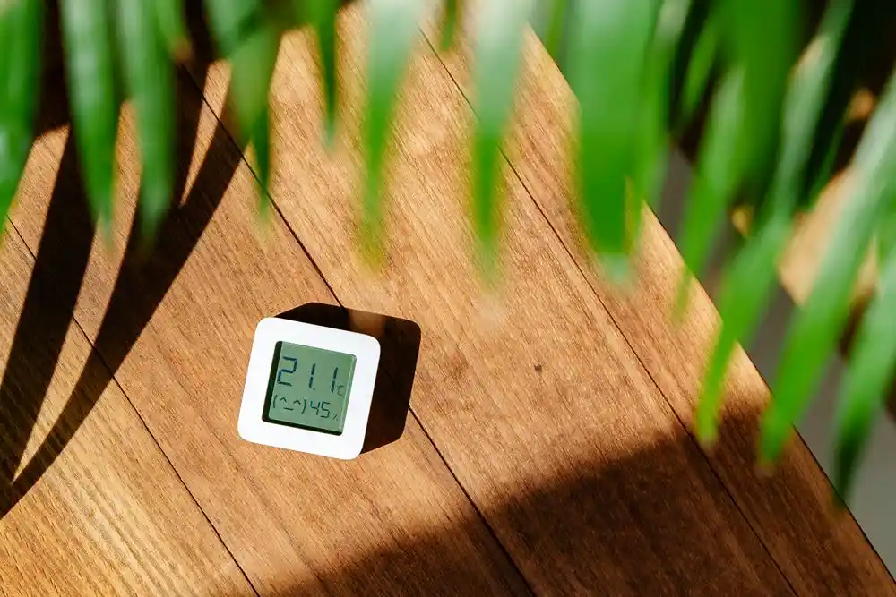 Ahşap masa üzerinde 21,1 °C sıcaklık ve nem gösteren dijital termometre bulunuyor