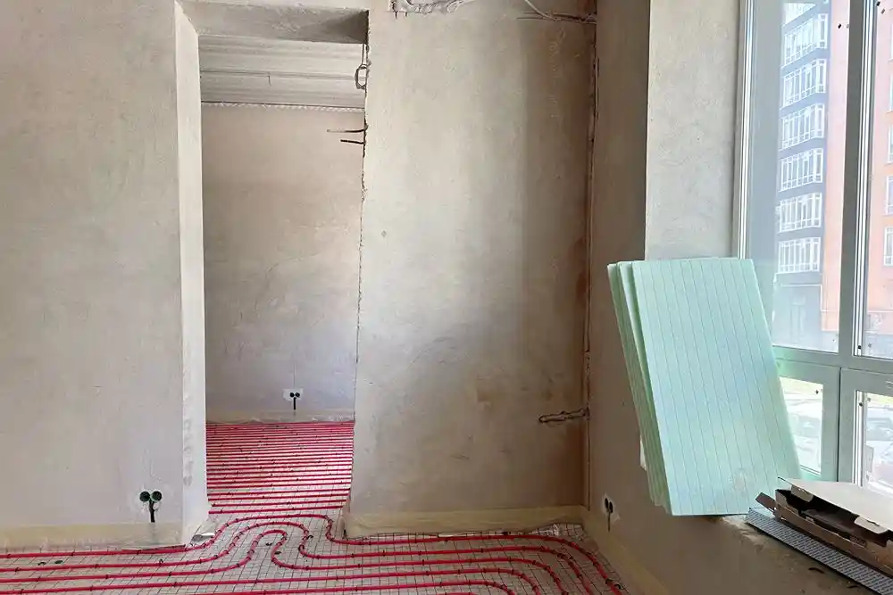 Tadilat halindeki odada zemine döşenmiş kırmızı yerden ısıtma boruları ve duvara yaslanmış yalıtım panelleri