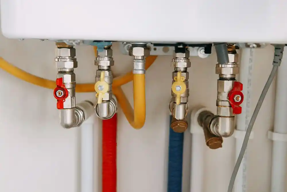 Kombinin altında çeşitli su ve gaz boruları ile kırmızı ve sarı vanalar görülüyor