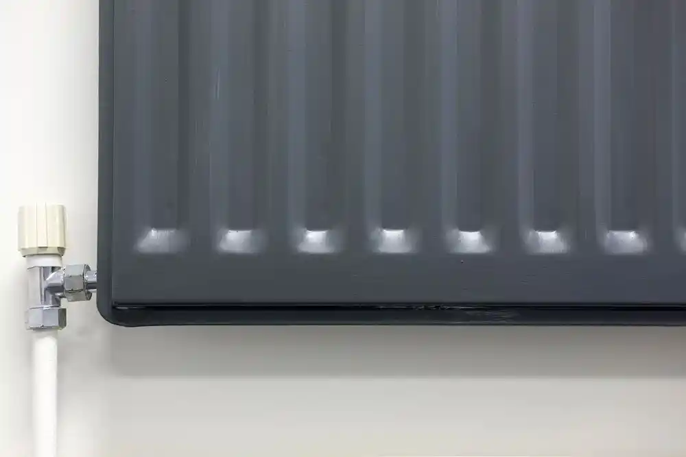 Duvara monte koyu renkli panel radyatör ve sol tarafındaki beyaz boru ile vana bağlantısı