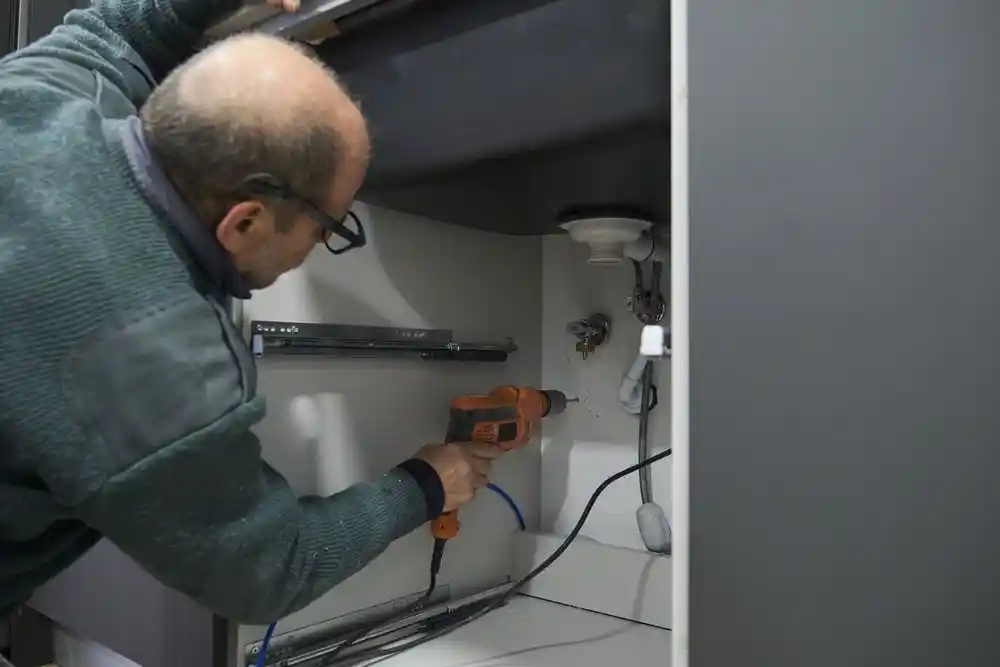 Bir adam dolabın iç kısmında elektrikli matkapla delik açıyor