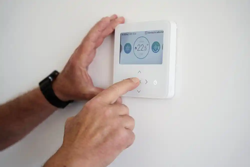 Bir kişi duvardaki termostatı ayarlıyor; ekranda 22,5 °C görülüyor