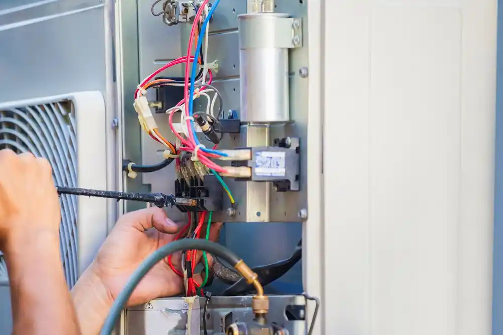 Bir kişi, klima ünitesinin açık elektrik bölümündeki kabloları tornavidayla onarıyor