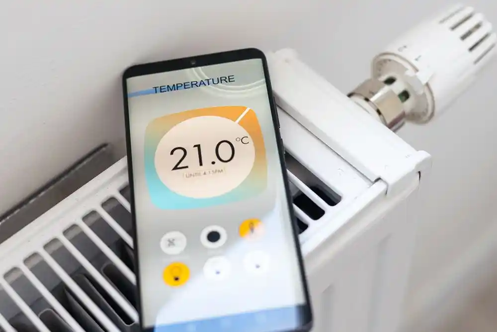 Radyatör üzerinde, ekranda 21,0 °C sıcaklık gösteren akıllı telefon ve termostatik vana
