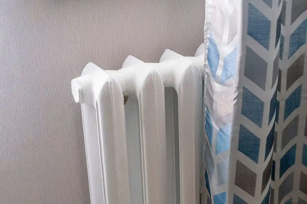 Desenli bir perdenin yanında beyaz panel radyatör