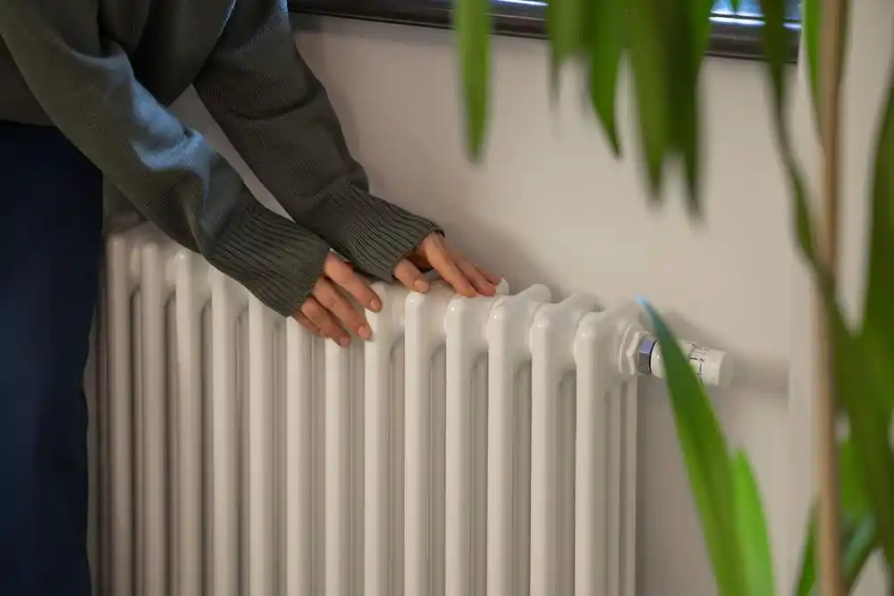 Bir kişi ellerini kalorifer peteğine uzatarak ısınmaya çalışıyor